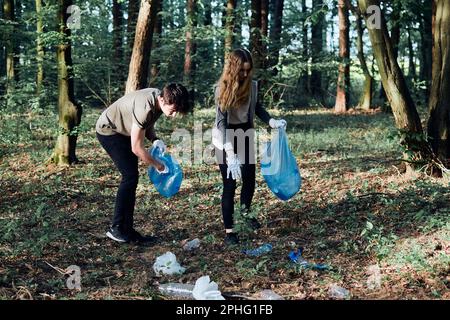 Junger Mann und Frau, die einen Wald aufräumen. Freiwillige sammeln Plastikabfälle in Säcke. Begriff der Kunststoffverschmutzung und zu viele Kunststoffabfälle. Umgebung Stockfoto