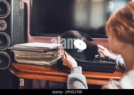 Junge Frau, die Musik von einem Plattenspieler hört. Retro- und Vintage-Musikstil. Mädchen mit analogem Plattenalbum sitzt zu Hause im Zimmer. Fema Stockfoto