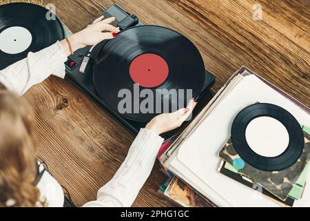 Junge Frau, die Musik von einem Plattenspieler hört. Wiedergabe von Musik auf Plattenspielern. Frau, die zu Hause Musik aus der alten Plattensammlung genießt. Stockfoto
