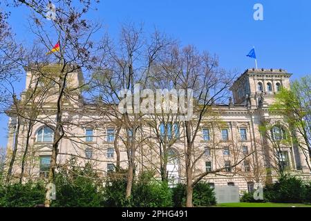 Park in der Nähe des Reichstags in Berlin. Hinter den Bäumen befinden sich die Kuppeln des Bundestags und die Flaggen Deutschlands und der Europäischen Union. Stockfoto