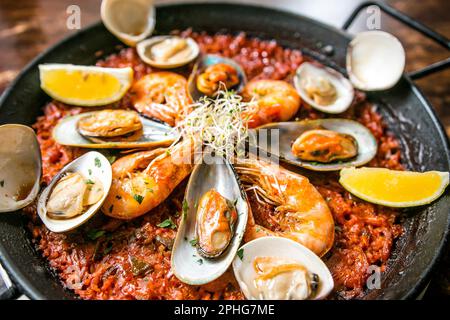 Meeresfrüchte-Paella mit Muscheln, Garnelen und Muscheln, serviert auf einer gusseisernen Pfanne mit Zitronenscheiben Stockfoto