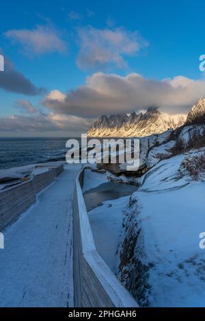 Am Fels sich brechende Wellen des Atlantik bei Tungeneset, Senja, Norwegen, mit den steilen Bergen Okshornan im Hintergrund. Stürmisches Winterwetter Stockfoto