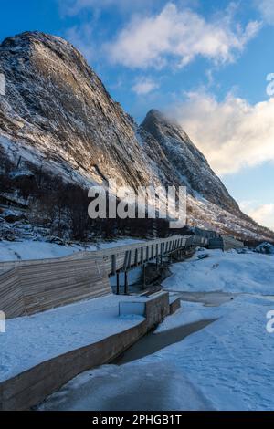 Am Fels sich brechende Wellen des Atlantik bei Tungeneset, Senja, Norwegen, mit den steilen Bergen Okshornan im Hintergrund. Stürmisches Winterwetter Stockfoto