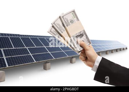 Männliche Hand hält Geld vor Solarpaneelen isoliert auf weißem Hintergrund Stockfoto