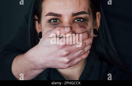 Die Hand eines Mannes bedeckt ihren Mund. Entführte Frau wird von einem Kerl bedroht Stockfoto