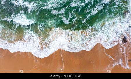 Drohnenansicht mit wunderschönen, nahtlosen Aufnahmen, während türkisfarbene Wellen an der sandigen Küste aufbrechen. Luftaufnahme des goldenen Strandes, der tiefes blaues Ozeanwasser und schaumige Wellen trifft Stockfoto