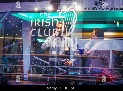 2015 - 03 Uhr Brisbane Australien - Straßenfotografie im Fenster des irischen Clubs - zwei Männer am Tisch am Fenster, die dunkles Bier trinken - Reflexionen der Stadt im Wind Stockfoto