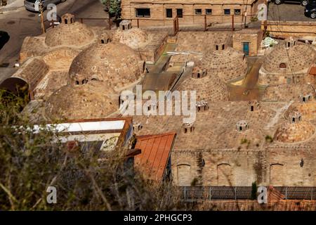 Gewölbte unterirdische Sulfur-Badehäuser mit Quellen, die Tiflis Georgia ihren Namen erhielt, indem sie von Nakata mit verschwommenem Unkraut im Vordergrund herabblickten Stockfoto