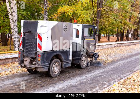 Die Straßenreinigungsmaschine auf einer Straße fegt im Herbst herabfallende Blätter. Kommunale Kraftfahrzeugausrüstung Stockfoto