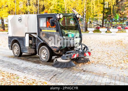 Die Straßenreinigungsmaschine auf einer Straße fegt im Herbst herabfallende Blätter. Kommunale Kraftfahrzeugausrüstung Stockfoto