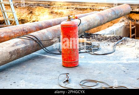 Rote Acetylenflasche mit Drucksensoren. Ausrüstung für das Schneiden von Metall mit Gas. Gasschweißanlage zum Schneiden von Metall auf einer Baustelle Stockfoto