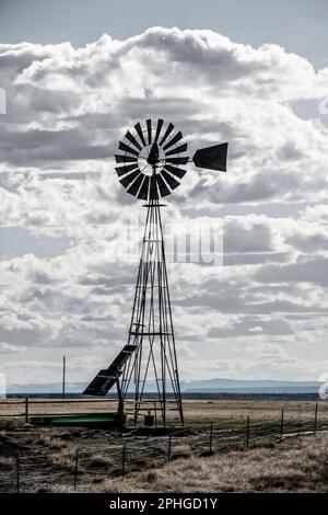 Windmühle in den Ebenen, angetrieben durch Solarpaneele mit Viehbewässerungsbecken durch Stacheldrahtzaun mit Bergen am Horizont - alte Sättigung entsättigt Stockfoto