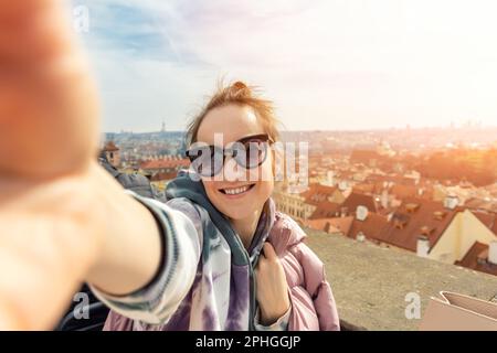 Poratrait einer jungen erwachsenen glücklichen Frau, die ein Foto-Selfie auf einer Reise nach prag macht, mit Panoramablick auf dem Dach der Altstadt bei sonnigen, warmen Sonnenuntergängen Stockfoto