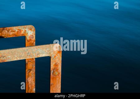 Rusty Metal Ladder on A Quay kontrastierte mit dem Blauen Meer, Mudeford Quay, Christchurch England, Großbritannien Stockfoto