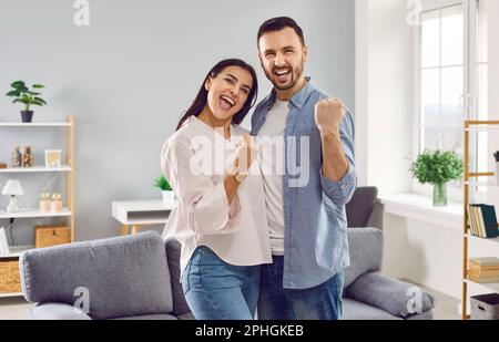 Glückliches, überfreuliches Paar Familie mit ja Geste, die im Wohnzimmer zu Hause stand. Stockfoto
