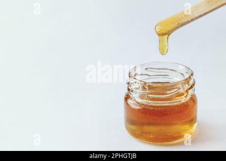 Flüssige gelbe Zuckerpaste in Glasgefäß, Holzspachtel auf weißem Hintergrund. Zucker. Enthaarung. Epilieren. Natürlicher Honig, Essen. Kopierraum. Stockfoto