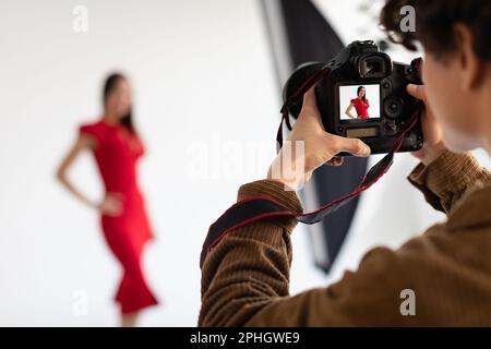 Professioneller männlicher Fotograf und hübsches weibliches Model in rotem Kleid, das im Studio schöne Bilder oder Inhalte fotografiert Stockfoto