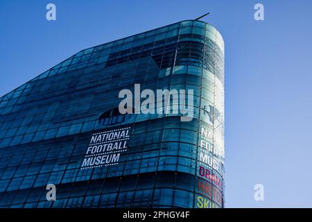 Der klare blaue Himmel verleiht dem Glasgebäude des National Football Museum in Manchester, England, einen blauen Farbton. Stockfoto