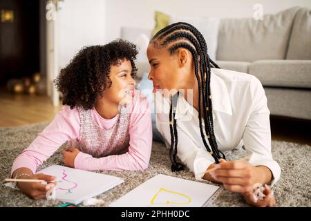 Lustige Afrikanische Mami Und Tochter, Die Ihre Zungen Ausstrecken Und Drinnen Zeichnen Stockfoto