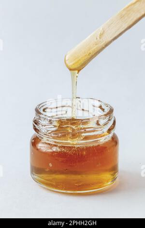 Flüssige gelbe Zuckerpaste in Glasgefäß, Holzspachtel auf weißem Hintergrund. Zucker. Enthaarung. Epilieren. Natürlicher Honig, Essen. Kopierraum. Stockfoto