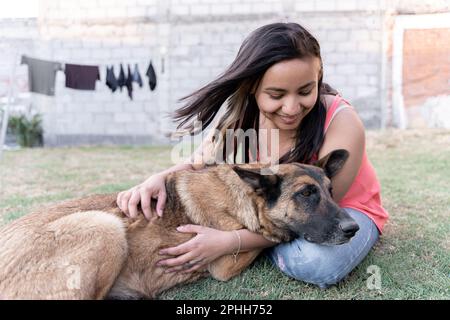Eine junge Hispanikerin umarmt ihren Hund im Garten, während sie Wäsche macht Stockfoto
