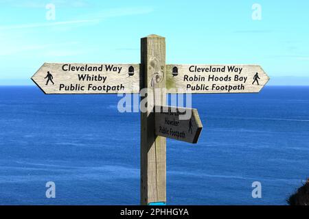 Ein Hinweisschild auf dem öffentlichen Fußweg Cleveland Way zwischen Whitby und Robin Hoods Bay mit dem Meer im Hintergrund Stockfoto