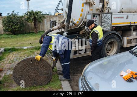 Kanalisationsarbeiter, die den Gullyschacht reinigen und die Kanalisation auf der Straße freimachen. Stockfoto