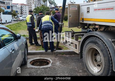 Kanalisationsarbeiter, die den Gullyschacht reinigen und die Kanalisation auf der Straße freimachen. Stockfoto