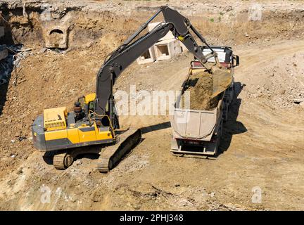 Bagger und Lkw arbeiten im Baugewerbe, beladen auf Lkw Stockfoto