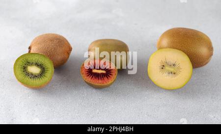 Verschiedene Kiwis liegen auf einem Stapel auf dem Tisch. Hälften roter, gelber und grüner Kiwi. Stockfoto