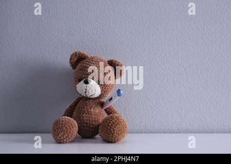 Niedlicher Spielzeugbär mit Thermometer auf weißem Tisch, Platz für Text. Kinderkrankenhaus Stockfoto