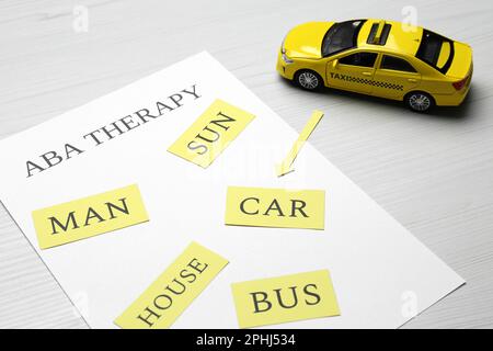 Taxifahrzeugmodell und Papierbogen mit Phrase ABA Therapie auf weißem Holztisch Stockfoto