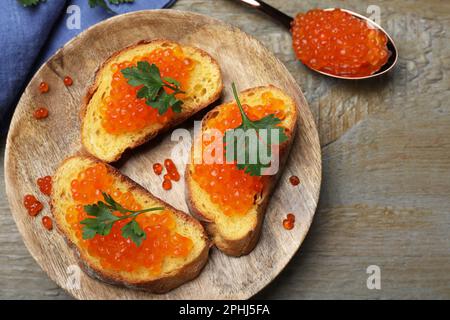 Köstliche Sandwiches mit rotem Kaviar und Petersilie auf einem Holztisch, flach liegend Stockfoto