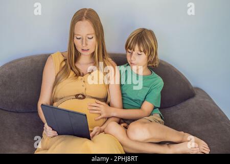 Schwangere mutter und Sohn sehen sich die Tablette an. Ein Buch lesen, einen Cartoon ansehen oder einen Videoanruf tätigen. Sehen Sie sich das Foto vom Ultraschall an Stockfoto