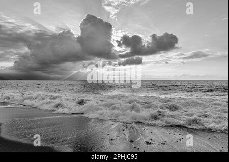 Ein Sonnenuntergang Am Meer Mit Sonnenstrahlen, Die Hinter Den Wolken Schwarz Und Weiß Ausstrahlen Stockfoto