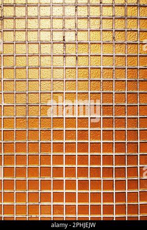 Die Gebäudewand ist mit kleinen quadratischen goldenen Fliesen dekoriert. Orangefarbene Glasfliesen in einem Swimmingpool. Strukturierter Hintergrund Stockfoto