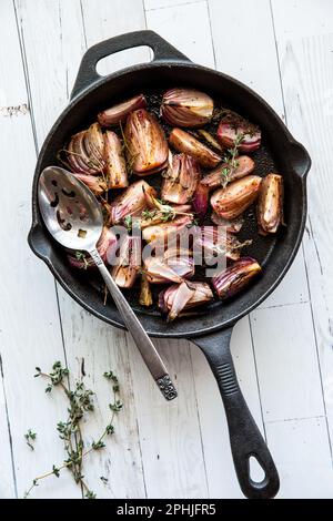 Im Ofen geröstete rote Zwiebeln mit Thymian in einer Gusseisenfritteuse. Stockfoto