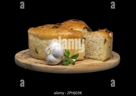 Rundes Focaccia-Brot mit Oliven, Knoblauch und Basilikumspalt auf schwarzem Hintergrund Stockfoto