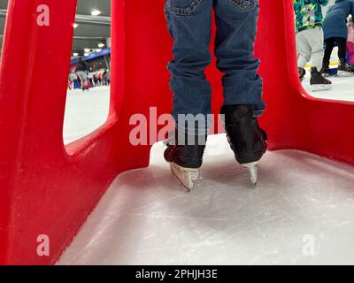 Einsteiger-Schlittschuhläufer mit einem Plastikläufer zur Unterstützung. Stockfoto