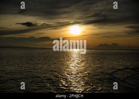 Malerischer Sonnenuntergang am Strand von Pamilacan Island auf den Philippinen, der wolkige Himmel leuchtet goldgelb. Stockfoto