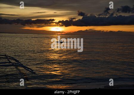 Malerischer Sonnenuntergang am Strand von Pamilacan Island auf den Philippinen, der wolkige Himmel glänzt goldgelb, ein Boot ist nah am Horizont. Stockfoto