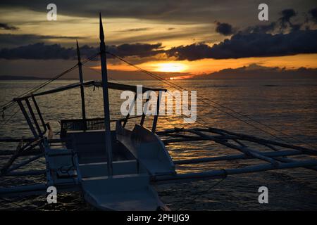 Malerischer Sonnenuntergang am Strand von Pamilacan Island auf den Philippinen, der wolkige Himmel scheint goldgelb, ein Boot ist auf dem Wasser. Stockfoto