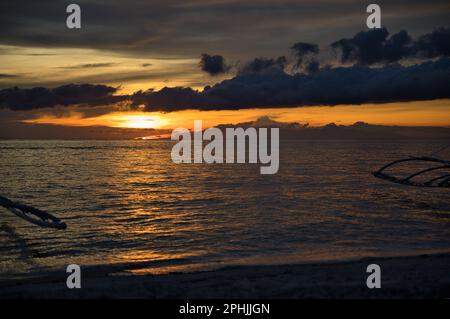 Malerischer Sonnenuntergang am Strand von Pamilacan Island auf den Philippinen, der wolkige Himmel leuchtet goldgelb. Stockfoto