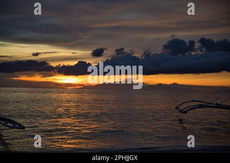 Malerischer Sonnenuntergang am Strand von Pamilacan Island auf den Philippinen, der wolkige Himmel leuchtet goldgelb. Stockfoto