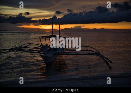 Malerischer Sonnenuntergang am Strand von Pamilacan Island auf den Philippinen, der wolkige Himmel scheint goldgelb, ein Boot ist auf dem Wasser. Stockfoto