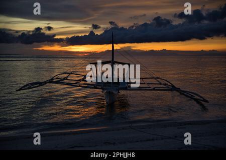 Malerischer Sonnenuntergang am Strand von Pamilacan Island auf den Philippinen, der wolkige Himmel scheint goldgelb, ein Boot ist auf dem Wasser. Stockfoto