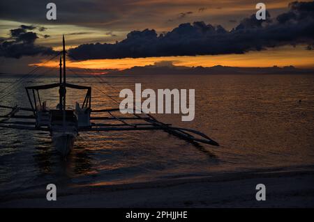 Malerischer Sonnenuntergang am Strand von Pamilacan Island auf den Philippinen, der wolkige Himmel scheint goldgelb, ein Boot ist auf dem Wasser. Stockfoto