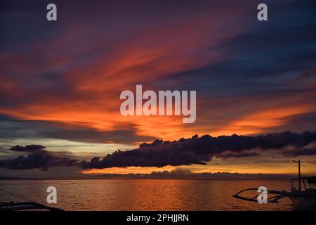 Malerischer Sonnenuntergang am Strand von Pamilacan Island auf den Philippinen, der wolkige Himmel leuchtet in goldenen Pfirsichfarben, Orange, Rot und Blau. Stockfoto