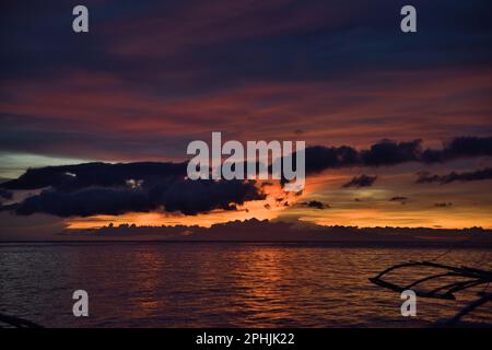 Malerischer Sonnenuntergang am Strand von Pamilacan Island auf den Philippinen, der wolkige Himmel leuchtet in goldenen Pfirsichfarben, Orange, Rot und Blau. Stockfoto