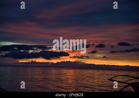 Malerischer Sonnenuntergang am Strand von Pamilacan Island auf den Philippinen, der wolkige Himmel leuchtet in goldenen Pfirsichfarben, Orange, Rot und Blau. Stockfoto